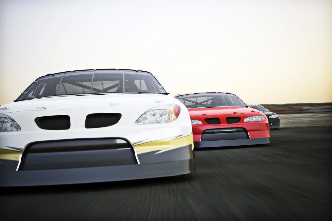 Two cars are racing on a track in the daytime.